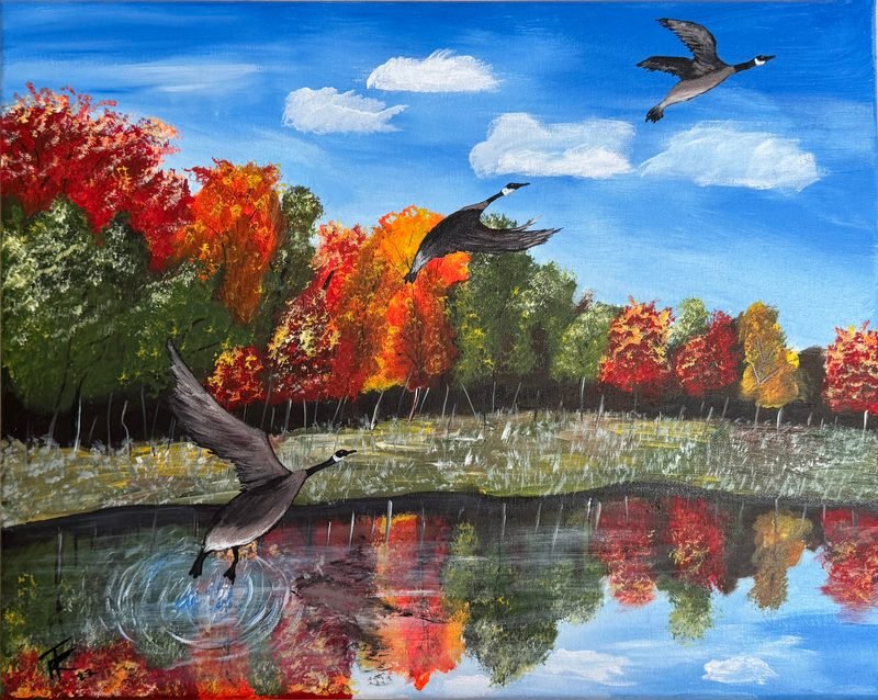 Canada geese flying low over a lake that reflects red and orange autumn trees