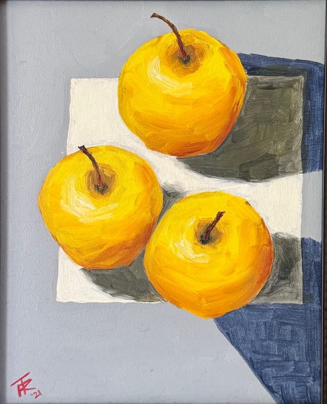 Three yellow apples on a white cloth over gray and blue