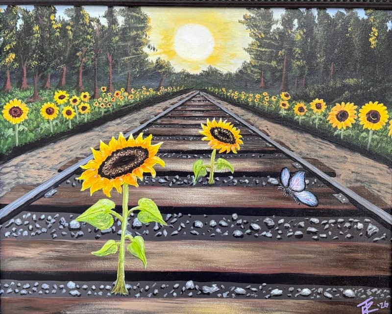 Sunflowers growing between the ties of a railroad track that runs toward a bright sun